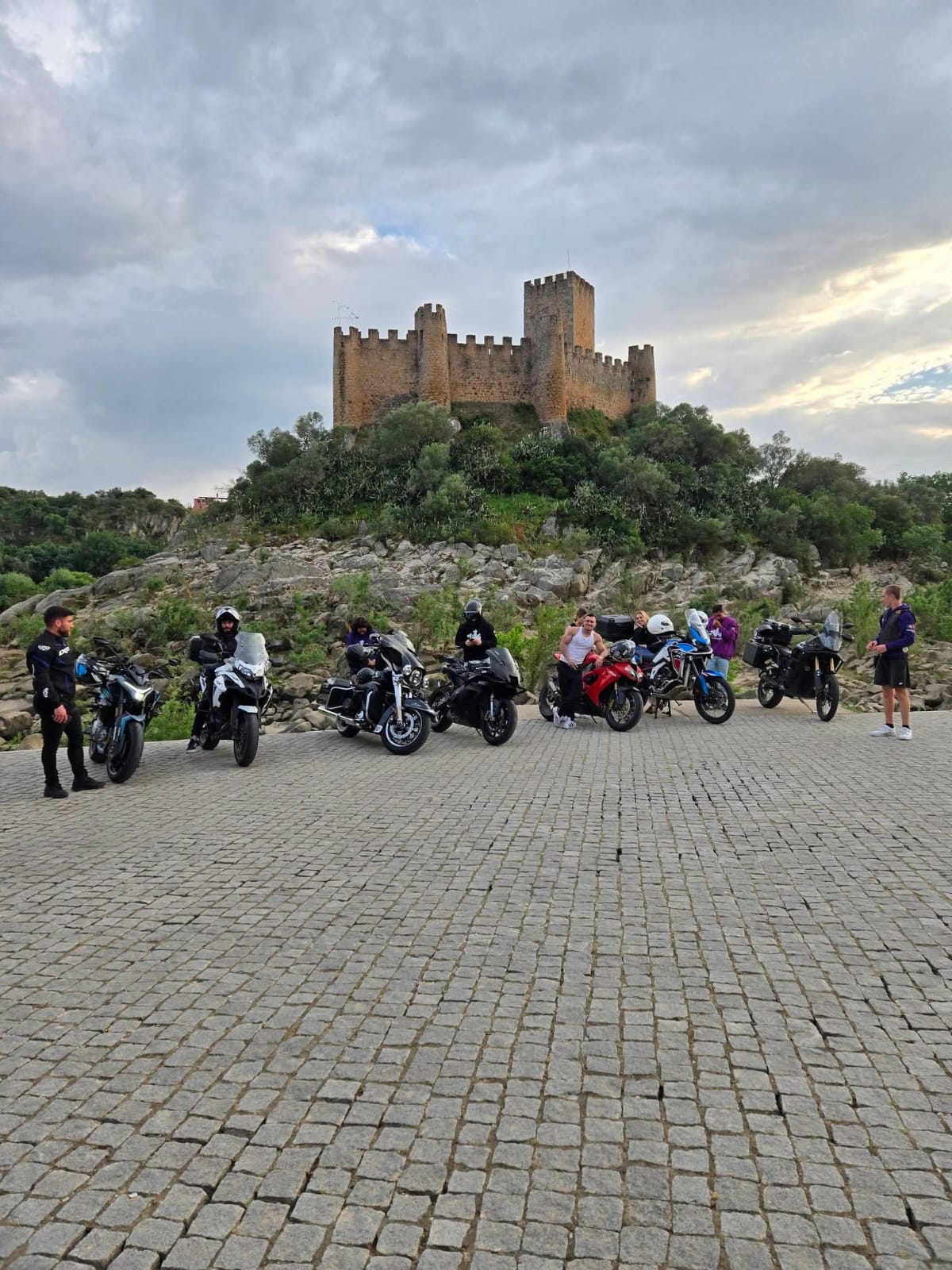 Grupo do clube com as motas ao pé de um castelo antigo no topo de uma colina rochosa